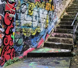 Laurence · 04/10/2025 · 2843 x 2479 Cette photographie met en scène un **escalier en béton** couvert de **graffitis colorés**. Le sujet principal est l’art urbain, avec des motifs variés et expressifs.La **composition** joue sur la perspective, guidant le regard vers le haut. Le **cadrage** serré accentue les détails des tags et des dégradations.Les **couleurs dominantes** sont vives : rouge, bleu, jaune, vert, créant un contraste avec le gris du béton. La **lumière** semble naturelle, tamisée, ajoutant une ambiance mystérieuse et légèrement mélancolique. Le style est **urbain et spontané**, évoquant une scène de rue dynamique et artistique.