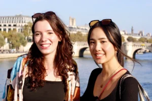 Cédric · 11/10/2025 · 4560 x 3040 Cette photographie met en scène deux femmes souriantes posant côte à côte. Le sujet principal est elles-mêmes, cadrées en plan serré. L’arrière-plan montre un pont emblématique et une rivière, suggérant un lieu urbain comme Paris.La lumière est naturelle et douce, probablement en journée. Les couleurs dominantes sont des tons chauds : teints de peau, vêtements clairs et contrastes avec les éléments architecturaux en arrière-plan.Le style est simple et spontané, évoquant une ambiance détendue et joyeuse.