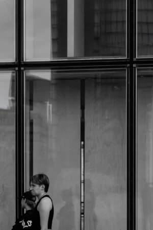 Philippe · 18/10/2025 · 2001 x 3000 Cette photographie en noir et blanc met en scène une personne comme sujet principal, vue de dos, penchée vers l’avant près d’une vitre. La composition joue sur les reflets et les lignes verticales des montants métalliques, créant une structure géométrique. Le cadrage serré et la lumière naturelle, tamisée et contrastée, accentuent une ambiance contemplative et mélancolique. Les tons gris dominent, renforçant l’aspect introspectif et moderne. Le style épuré et minimaliste évoque une atmosphère urbaine et intime, mêlant solitude et réflexion.