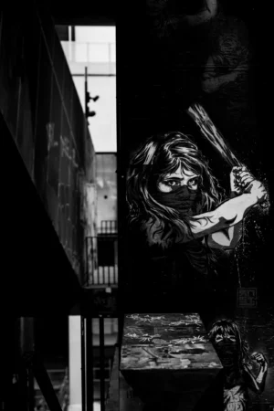 Philippe · 18/10/2025 · 2001 x 3000 Cette photographie en noir et blanc met en scène une silhouette féminine allongée sur un mur, en position fœtale, le visage caché. Le sujet principal est cette figure solitaire et mélancolique.La composition joue sur les contrastes entre ombre et lumière, avec un cadrage serré qui isole la personne. Les lignes architecturales du bâtiment en arrière-plan renforcent une ambiance urbaine et désolée. La lumière, tamisée et contrastée, accentue les textures et les ombres, créant une atmosphère sombre et contemplative. Le style est artistique et dramatique, évoquant une solitude poétique et une certaine tristesse.