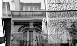 Pascale · 18/10/2025 · 2000 x 1204 Cette photographie en noir et blanc met en scène une façade architecturale ancienne. Le sujet principal est une entrée monumentale avec une arche et des balcons en fer forgé. La composition joue sur les contrastes entre les textures lisses et rugueuses des murs, ainsi que les jeux d'ombres et de lumière.Le cadrage serré isole partiellement les éléments architecturaux, créant une ambiance mystérieuse et intemporelle. Les tons gris dominent, accentuant les détails et les jeux de lumière naturelle. Le style rappelle le réalisme photographique classique, évoquant une atmosphère à la fois sobre et élégante.