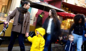 Pascale · 04/10/2025 · 2000 x 1203 Cette photographie capture une scène de rue animée. Le sujet principal semble être un enfant en veste jaune vif, entouré d’adultes. La composition montre un groupe en mouvement, avec un cadrage légèrement serré sur les visages et les tenues colorées.La lumière est naturelle, probablement en journée, avec des tons doux mais contrastés. Les couleurs dominantes sont les teintes automnales (beige, marron) et les couleurs vives des vêtements (jaune, bleu). Le style est documentaire, reflétant une ambiance quotidienne et chaleureuse dans un cadre urbain.