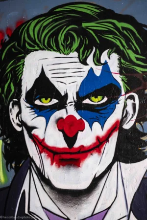 Benoit · 04/10/2025 · 5037 x 7556 Cette photographie représente le Joker, personnage emblématique de DC Comics. Le sujet principal est son visage stylisé, avec un maquillage coloré : peau verte, sourire rouge et yeux jaunes. La composition est centrée sur ce visage, avec un cadrage serré qui isole le personnage. Les couleurs dominantes sont le vert, le rouge et le bleu, créant un contraste marqué. Le style est graphique et caricaturé, évoquant une esthétique de dessin animé ou de bande dessinée. L’ambiance est à la fois inquiétante et théâtrale, renforcée par les couleurs vives et les traits exagérés.
