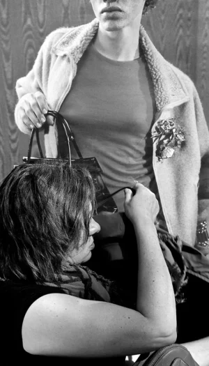 Franck T. · 04/10/2025 · 571 x 1000 Cette photographie en noir et blanc montre deux personnes, dont une enfant assise à l'avant-plan, les yeux fermés, tandis qu'une personne debout, probablement un adulte, semble lui ajuster ou observer quelque chose sur sa tête, peut-être un accessoire ou un appareil.La composition est serrée, centrée sur les deux sujets. Le cadrage est rapproché, mettant l'accent sur l'interaction entre eux. La lumière est douce et naturelle, créant des contrastes modérés. L'absence de couleurs renforce l'aspect intemporel et intime de la scène, évoquant une ambiance à la fois quotidienne et nostalgique.