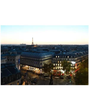 Cette photographie montre une vue panoramique de Paris, probablement prise depuis un point élevé. Le **sujet principal** est la ville avec ses bâtiments emblématiques, dont la **Tour Eiffel** au loin.La **composition** est équilibrée, avec des architectures variées et des rues animées. Le **cadrage** est large, capturant une étendue urbaine. La **lumière** est douce, typique d’un coucher de soleil, créant une ambiance chaleureuse. Les **couleurs dominantes** sont des tons neutres (beige, gris) adoucis par des éclairages artificiels jaunes et des touches de vert des arbres.Le **style** est réaliste et documentaire, évoquant une **ambiance** paisible et élégante, caractéristique des soirées parisiennes.