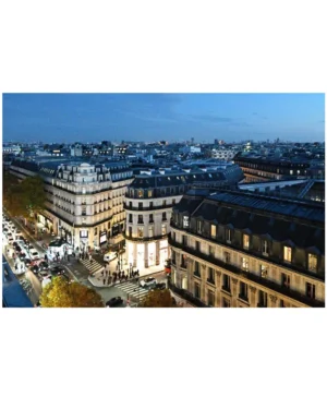 Cette photographie montre une vue aérienne d’un quartier urbain, probablement parisien. Le sujet principal est une perspective architecturale classique avec des immeubles haussmanniens alignés.La composition est symétrique et ordonnée, avec une avenue centrale bordée d’arbres et de bâtiments. Le cadrage large capture une étendue de la ville jusqu’à l’horizon. La lumière est douce, typique d’un coucher ou lever de soleil, créant des ombres longues et une ambiance chaleureuse. Les couleurs dominantes sont les tons beiges, gris et bleus, renforçant l’élégance et la sérénité du lieu. Le style est photographique et urbain, évoquant une ambiance paisible et intemporelle.