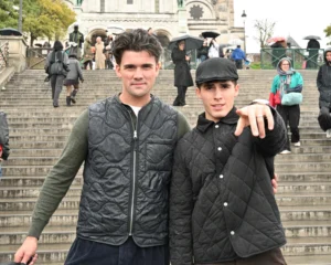 Mary · 15/11/2025 · 2784 x 2227 Cette photographie met en scène deux jeunes hommes posant sur un escalier en pierre. Ils forment le sujet principal, vêtus de vestes en cuir texturé, avec une ambiance décontractée et urbaine.La composition est symétrique, avec un cadrage serré sur eux, bien que l’arrière-plan montre des passants et des bâtiments. La lumière semble naturelle, probablement en journée, avec des tons doux. Les couleurs dominantes sont les teintes neutres (gris, noir, beige) et quelques touches de vert et de bleu dans l’arrière-plan.Le style est réaliste et spontané, évoquant une ambiance moderne et citadine.