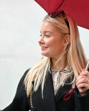 Mary · 15/11/2025 · 2053 x 2567 Cette photographie met en scène une femme blonde comme sujet principal. Elle porte un manteau noir et tient un parapluie rouge. Le cadrage est serré sur son visage et le haut de son corps, avec un léger flou d’arrière-plan.La lumière semble naturelle et douce, éclairant son visage de manière homogène. Les couleurs dominantes sont les tons froids (noir, gris) contrastant avec le rouge vif du parapluie. Le style est sobre et élégant, évoquant une ambiance urbaine et moderne, avec une touche de fraîcheur et de dynamisme.
