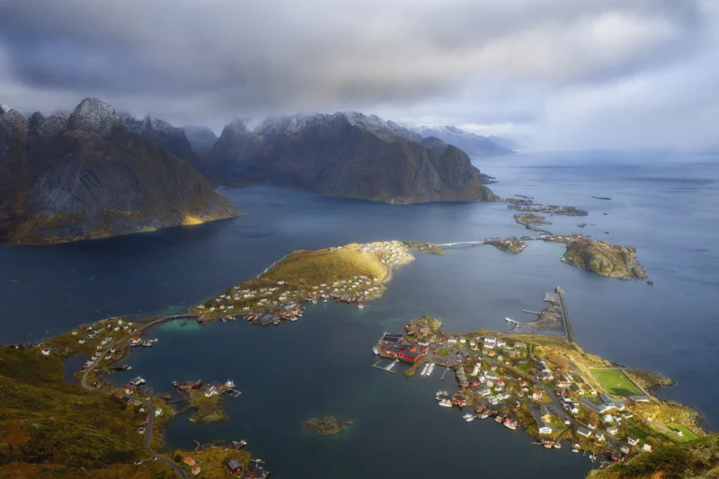 Ahmet · 22/10/2022 · 3000 x 2000 Cette photographie montre les îles **Lofoten**, en Norvège. Le **sujet principal** est un paysage côtier spectaculaire avec des montagnes escarpées et des villages de pêcheurs colorés.La **composition** est aérée, avec une vue aérienne offrant une perspective large sur les îles et le fjord. Le **cadrage** inclut des éléments naturels et humains en harmonie.La **lumière** semble douce, légèrement voilée par des nuages, créant une ambiance sereine. Les **couleurs dominantes** sont les verts des montagnes, les bleus profonds de l’eau et les teintes vives des maisons.Le **style** est réaliste et photographique, évoquant une **ambiance** paisible et majestueuse, typique des paysages nordiques.