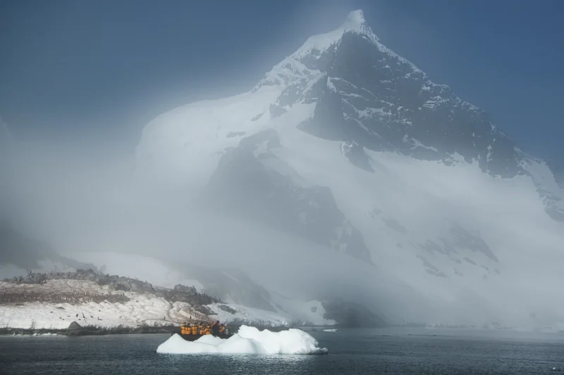 Ahmet · 16/12/2023 · 3000 x 2000 Cette photographie met en scène un **montagne enneigée**, probablement un sommet himalayen, partiellement enveloppé dans un épais brouillard. Le **sujet principal** est la cime majestueuse, émergente des nuages bas.La **composition** joue sur le contraste entre la montagne et le ciel voilé, créant une impression de mystère. Le **cadrage** est serré, centré sur le pic, avec une perspective dramatique.La **lumière** est douce et diffuse, adoucissant les contours. Les **couleurs dominantes** sont le blanc de la neige et les teintes bleutées du ciel, renforçant une **ambiance** glaciale et onirique, presque surnaturelle. Le style est **réaliste et poétique**.