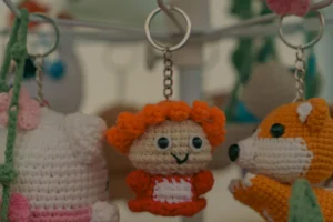 Don · 5350 x 3567 Cette photographie met en scène des **peluches crochetées** comme sujet principal. La composition montre trois petits animaux suspendus à un support, avec un cadrage serré sur l’un d’eux, un singe orange souriant.La lumière est douce et naturelle, éclairant les détails des peluches. Les **couleurs dominantes** sont vives : orange, blanc et touches de rose et bleu. Le style est artisanal et mignon, évoquant un travail fait main. L’ambiance est chaleureuse et ludique, rappelant des jouets d’enfants ou des créations décoratives.