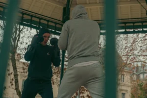 Don · 5079 x 3386 Cette photographie montre deux individus en train de s'affronter dans une cage, probablement pour un combat de rue ou un sport de combat.**Sujet principal** : Les deux combattants, l’un en position offensive, l’autre en défense.
**Composition** : Cadrage serré sur la cage, avec un arrière-plan flou de bâtiments et de branches.
**Lumière** : Naturelle, tamisée, créant des ombres marquées.
**Couleurs dominantes** : Teintes neutres (gris, noir, beige) avec des touches de vert et de brun.
**Style** : Réaliste et dynamique, évoquant un moment intense.
**Ambiance** : Tension, confrontation et urgence.