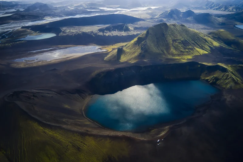 Ahmet · 27/08/2023 · 3000 x 1998 Cette photographie capture un paysage volcanique spectaculaire. Le sujet principal est un cratère rempli d’eau turquoise, entouré de terrains arides et de montagnes verdoyantes.La composition est équilibrée, avec le cratère au centre et les montagnes en arrière-plan. Le cadrage aérien offre une vue panoramique. La lumière naturelle, douce et diffuse, met en valeur les contrastes. Les couleurs dominantes sont les verts, les bleus profonds et les tons terreux.Le style est documentaire et naturel, évoquant une ambiance à la fois sauvage et paisible, presque mystique.