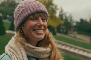 Don · 5991 x 3994 Cette photographie met en scène une femme souriante comme sujet principal, vêtue d’un bonnet et d’un écharpe. Le cadrage est serré sur son visage, avec un arrière-plan flou montrant des arbres et un chemin.La lumière est douce et naturelle, probablement en journée. Les couleurs dominantes sont les tons chauds (beige, marron) et les teintes pastel (violet du bonnet, bleu du ciel). Le style est simple et spontané, évoquant une ambiance chaleureuse et détendue, presque automnale. L’expression joyeuse de la femme ajoute une touche conviviale à la scène.