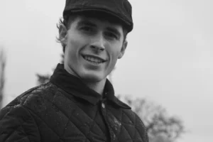 Don · 3686 x 2457 Cette photographie en noir et blanc met en scène un jeune homme comme sujet principal, souriant légèrement. Le cadrage est serré sur son visage et le haut de son torse, avec un fond flou et légèrement déstructuré.La lumière est douce et naturelle, éclairant son visage de manière homogène. Les couleurs dominantes sont les nuances de gris, typiques du noir et blanc, renforçant une ambiance sobre et intemporelle.Le style est simple et direct, évoquant une touche documentaire ou artistique classique. L’ambiance est chaleureuse et authentique, avec une impression de simplicité et de naturel.