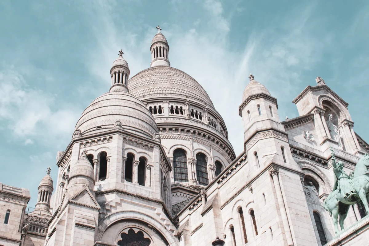Deniz · 31/05/2025 · 2048 x 1365 Cette photographie met en scène le **Sacré-Cœur de Montmartre** à Paris. Le **sujet principal** est la basilique, avec ses deux dômes blancs et sa façade néoromane. La **composition** est centrée sur ces éléments architecturaux majestueux, avec un **cadrage serré** qui accentue la verticalité et la grandeur des tours.La **lumière** est douce, légèrement voilée, créant une ambiance sereine. Les **couleurs dominantes** sont les tons **beiges, blancs et gris**, adoucis par un ciel bleu pâle. Le **style** est épuré, presque vintage, avec un léger flou artistique. L’**ambiance** est paisible et spirituelle, évoquant sérénité et élévation.