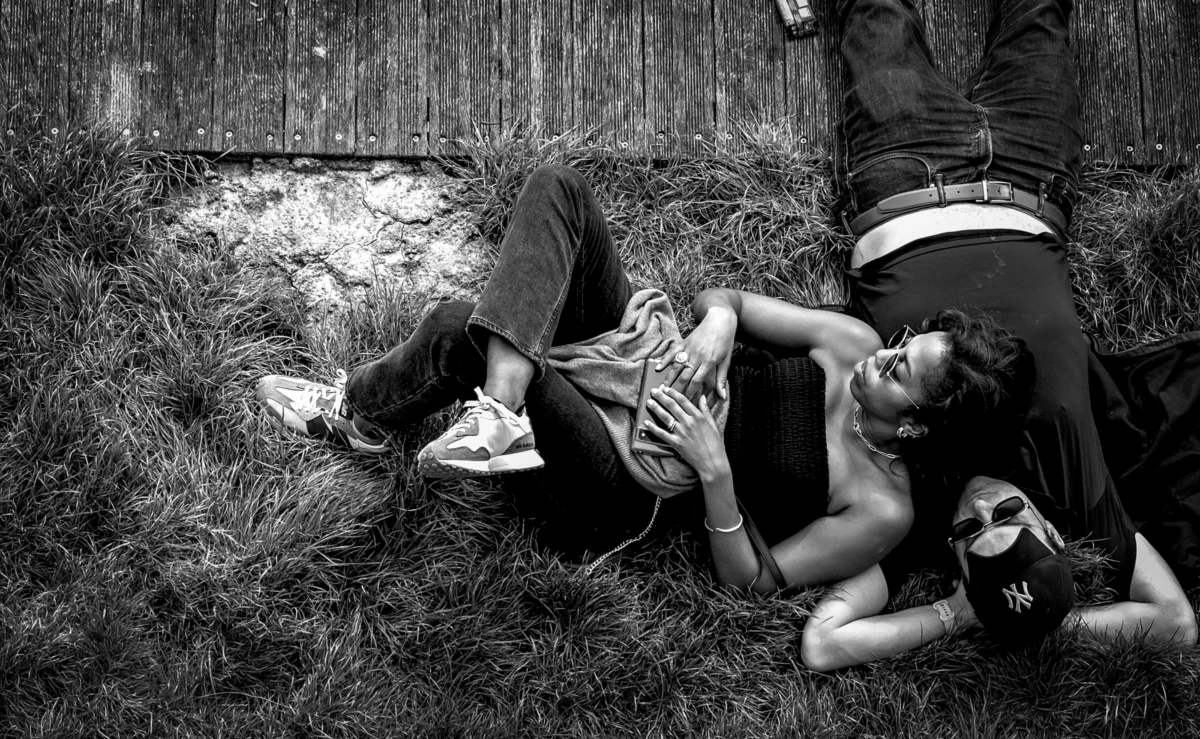 AnJo · 06/04/2024 · 4000 x 2461 Cette photographie en noir et blanc montre deux jeunes personnes allongées dans un champ d'herbe sèche. Le sujet principal est leur posture détendue et complice, presque théâtrale.La composition est dynamique, avec un cadrage serré qui isole les sujets. La lumière naturelle, douce mais contrastée, accentue les ombres et les textures. Les couleurs dominantes, bien que monochromes, jouent sur les nuances de gris et de noir.Le style est artistique et spontané, évoquant une ambiance à la fois naturelle et intime, presque mélancolique.