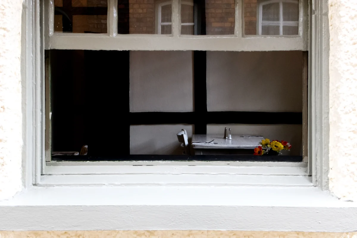 AnJo · 12/07/2015 · 4896 x 3264 Cette photographie montre un intérieur vu à travers une fenêtre à petits carreaux. Le sujet principal est une pièce sombre avec un miroir reflétant une partie de la fenêtre et un vase contenant des fleurs jaunes.La composition est symétrique et centrée, avec un cadrage serré sur la fenêtre. La lumière est naturelle et tamisée, créant des contrastes doux. Les couleurs dominantes sont les tons gris et noirs de la pièce, adoucis par les touches de jaune des fleurs.Le style est sobre et minimaliste, évoquant une ambiance calme et introspective.