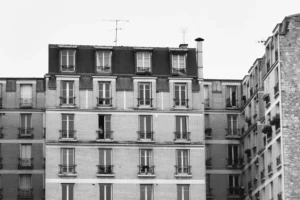 Deniz · 22/11/2025 · 2733 x 1822 Cette photographie en noir et blanc met en scène une façade d’immeubles parisiens typiques. Le sujet principal est une série d’appartements alignés, avec leurs balcons et fenêtres.La composition est symétrique et verticale, soulignant la répétition architecturale. Le cadrage est serré, centré sur les bâtiments sans éléments distractifs.La lumière est douce et uniforme, sans contrastes marqués, renforçant l’aspect monochrome. Les tons dominants varient du gris clair au noir, créant une ambiance sobre et intemporelle. Le style évoque un réalisme documentaire, évoquant une atmosphère urbaine calme et mélancolique.