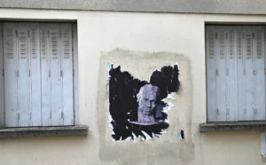 Pierre · 22/11/2025 · 4980 x 3093 Cette photographie montre un graffiti comme sujet principal, représentant un visage stylisé avec des traits anguleux et une coiffure en forme de flammes. La composition est simple, centrée sur le graffiti encadré par deux fenêtres à barreaux fermées.Le cadrage est serré, mettant en valeur le détail du mural. La lumière semble naturelle, éclairant uniformément la scène sans ombres marquées. Les couleurs dominantes sont des teintes grises et bleutées, avec des touches de noir et blanc pour le graffiti. Le style est urbain et artistique, évoquant une ambiance à la fois mystérieuse et rebelle.