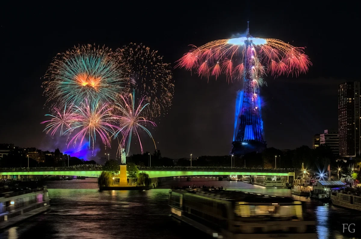 Frédéric · 14/07/2023 · 1630 x 1080 Cette photographie capture un spectacle de **feux d'artifice** nocturne. Le **sujet principal** est les explosions colorées illuminant le ciel. La **composition** montre une vue large avec des motifs circulaires et éclatants, encadrée par des structures urbaines en arrière-plan.Le **cadrage** est horizontal, offrant une perspective immersive. Les **lumières** sont vives et contrastées, créant une ambiance dynamique. Les **couleurs dominantes** sont des teintes vives : bleu, rouge, vert et jaune.Le **style** est photographique, avec un flou d'arrière-plan pour accentuer les éclats lumineux. L’**ambiance** est festive et magique, évoquant une célébration nocturne.