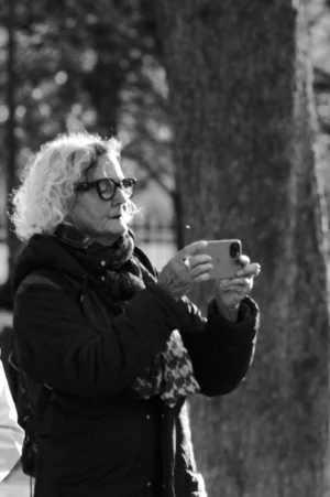 Thomas · 01/11/2025 · 1080 x 1625 Cette photographie en noir et blanc met en scène un homme âgé comme sujet principal, vêtu d'un manteau et portant des lunettes. Il tient une tasse près de son visage, comme s'il s'apprêtait à boire.La composition est simple et naturelle, avec un cadrage serré sur le sujet, laissant peu de place aux éléments de fond, principalement des arbres. La lumière semble douce et naturelle, créant des contrastes modérés. L'absence de couleurs renforce l'atmosphère intemporelle et contemplative, évoquant une ambiance calme et mélancolique. Le style est documentaire et sobre.
