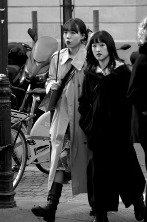 Thomas · 01/11/2025 · 1080 x 1625 Cette photographie en noir et blanc met en scène deux jeunes femmes comme sujets principaux, marchant côte à côte. La composition est dynamique, avec un cadrage serré sur elles, les plaçant au premier plan. L’arrière-plan montre des vélos et un trottoir, suggérant une ambiance urbaine.La lumière est naturelle, douce et légèrement contrastée, accentuant les contours. Les couleurs dominantes, bien que monochromes, jouent sur les nuances de gris et de noir, renforçant l’atmosphère rétro ou cinématographique. Le style évoque un réalisme intemporel, avec une ambiance à la fois moderne et nostalgique.