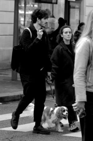 Thomas · 01/11/2025 · 1080 x 1625 Cette photographie en noir et blanc met en scène un homme comme sujet principal, marchant sur un passage piéton tout en tenant un objet à la main. La composition est dynamique, avec un cadrage serré sur lui et son chien qui le suit.L’ambiance est urbaine et spontanée. La lumière semble naturelle, probablement en journée, avec des contrastes marqués. Le style est documentaire, capturant un moment authentique de la vie quotidienne. Les tons gris dominent, renforçant l’aspect réaliste et intemporel de la scène.