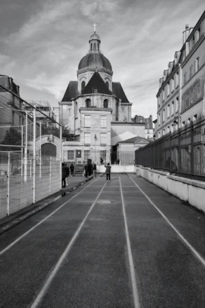 Philippe · 01/11/2025 · 2001 x 3000 Cette photographie met en scène une **architecture urbaine historique** avec une **cathédrale ou un édifice religieux** à dôme central en sujet principal. La **composition** est symétrique, avec une **perspective axiale** menant vers le bâtiment.Le **cadrage** est serré sur une allée pavée, encadrée par des bâtiments. La **lumière** est douce, typique d’un jour couvert, créant des contrastes modérés. Les **couleurs dominantes** sont en noir et blanc, accentuant les textures et les jeux d’ombres.Le **style** est documentaire et esthétique, évoquant une **ambiance mélancolique et intemporelle**, presque onirique.