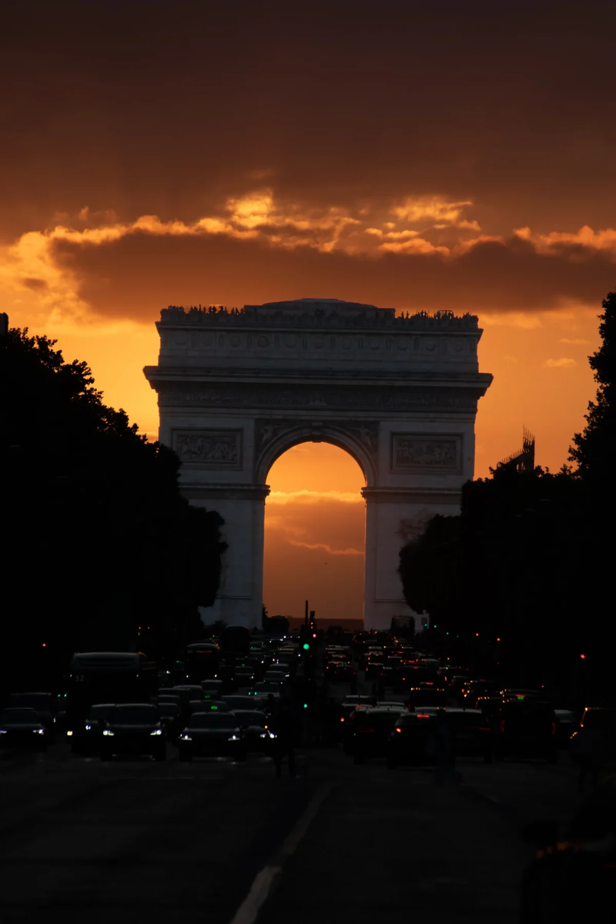 Tery · 4275 x 6413 Cette photographie met en scène l’**Arc de Triomphe** à Paris, sujet principal. La composition est axée sur l’axe central de la voie des Champs-Élysées, avec un cadrage serré qui isole l’arc.La lumière dorée du coucher de soleil crée un **contre-jour** dramatique, soulignant les contours de l’arc. Les **couleurs dominantes** sont des tons chauds (oranges, rouges) contrastant avec le noir de la silhouette.Le style est **photojournalistique et poétique**, évoquant une ambiance **sublime et contemplative**, mêlant grandeur historique et émotion.