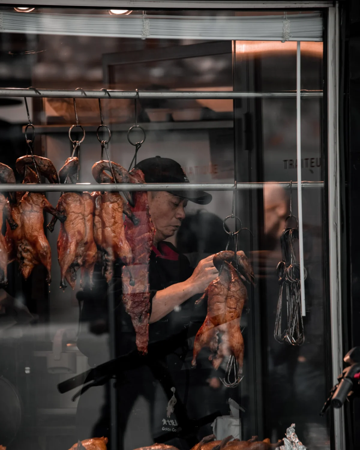 Tery · 4480 x 5600 Cette photographie met en scène des **animaux suspendus**, probablement des carcasses d'animaux, dans un espace industriel ou un abattoir. Le **sujet principal** semble être le processus de préparation ou de découpe.La **composition** est symétrique, avec des carcasses alignées verticalement. Le **cadrage** est serré, centré sur les animaux et les mains d’un travailleur. La **lumière** est froide et artificielle, créant des contrastes nets. Les **couleurs dominantes** sont des tons rouges et bruns, renforçant l’aspect organique et brut.Le **style** est documentaire et réaliste, évoquant une **ambiance industrielle et crue**, presque clinique.