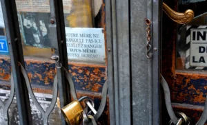 Pascale · 08/11/2025 · 1000 x 607 Cette photographie montre des **portes métalliques fermées** avec plusieurs **cadenaș (loquets)** rouillés et des **affiches partiellement déchirées**.La **composition** est serrée, avec un cadrage en gros plan. La **lumière** semble naturelle mais tamisée, créant des ombres marquées. Les **couleurs dominantes** sont des tons froids (gris, métal oxydé) contrastant avec des touches de rouge et d’orange sur les affiches.Le style est **documentaire et réaliste**, évoquant une ambiance **abandonnée, interdite ou nostalgique**, typique d’un lieu peu fréquenté ou protégé.