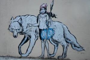 Vera · 22/11/2025 · 6213 x 4142 Cette photographie montre un mural urbain représentant une enfant montée sur un loup. Le sujet principal est ce duo, évoquant une scène fantastique ou mythique. La composition est dynamique, avec un cadrage serré mettant en valeur les deux figures.Les couleurs dominantes sont des teintes bleutées et grises, avec des touches de rouge et de bleu pour les détails. Le style est celui du street art, aux traits stylisés et simplifiés. L’ambiance est à la fois mystérieuse et poétique, renforcée par un éclairage naturel doux.
