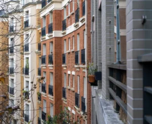 Laurent · 2649 x 2160 Cette photographie montre une façade urbaine avec des immeubles en enfilade. Le sujet principal est une série d'appartements aux balcons et fenêtres variées, dont les couleurs dominantes sont les tons beiges, bruns et ocres.La composition est verticale et serrée, mettant en valeur les lignes architecturales. Le cadrage est serré, accentuant la profondeur et les détails des bâtiments. La lumière semble naturelle, douce et légèrement tamisée, créant une ambiance calme et un peu mélancolique. Le style est réaliste et documentaire, reflétant une esthétique urbaine classique.