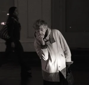 Pascale · 20/12/2025 · 1000 x 953 Cette photographie en noir et blanc met en scène une femme âgée comme sujet principal, tenant un téléphone à son oreille. La composition est simple, avec un cadrage serré sur elle, légèrement de trois-quarts.L’ambiance est intimiste et nocturne, éclairée par une lumière douce et tamisée, créant des contrastes marqués. Les couleurs dominantes, bien que monochromes, jouent sur les nuances de gris et de noir, renforçant l’atmosphère contemplative et mélancolique. Le style est documentaire et réaliste, capturant un moment de vie quotidienne avec authenticité.