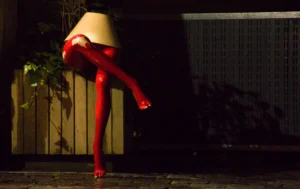 Pascale · 20/12/2025 · 1000 x 631 Cette photographie met en scène une personne vêtue d’une combinaison rouge transparente et d’un chapeau en forme de seau à glace. Le sujet principal semble en mouvement, capturant une posture dynamique.La composition est épurée, avec un cadrage serré qui isole le personnage sur un fond sombre et flou. La lumière, tamisée et contrastée, accentue les contours du sujet et crée une ambiance mystérieuse. Les couleurs dominantes sont le rouge vif de la combinaison et les tons sombres de l’arrière-plan.Le style évoque une touche artistique et surréaliste, renforcée par l’éclairage dramatique. L’ambiance est à la fois énigmatique et théâtrale.