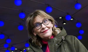 Pascale · 06/12/2025 · 1250 x 751 Cette photographie met en scène une femme comme sujet principal, souriante, avec des lunettes rondes et vêtue d’un manteau vert et d’un pull rouge. Le cadrage est serré, centré sur son visage.L’arrière-plan est composé de motifs géométriques lumineux en bleu. La lumière est douce et met en valeur son visage, créant un contraste avec les teintes vives de l’arrière-plan. Les couleurs dominantes sont le bleu électrique, le vert et le rouge, apportant une ambiance moderne et joyeuse. Le style est épuré et contemporain, évoquant une touche artistique et dynamique.