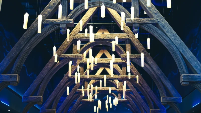 Romain · 19/02/2024 · 2048 x 1152 Cette photographie montre un intérieur architectural impressionnant, probablement une cathédrale ou une église gothique. Le sujet principal est l'arche voûtée richement décorée, avec des structures en bois et des éléments lumineux suspendus.La composition met en valeur la symétrie et la hauteur des voûtes. Le cadrage est serré, centré sur les détails architecturaux et les jeux de lumière. Les couleurs dominantes sont des bleus profonds et des tons chauds dorés, créant un contraste saisissant.Le style est épuré et dramatique, renforcé par une lumière artificielle qui accentue l'ambiance mystique et majestueuse.