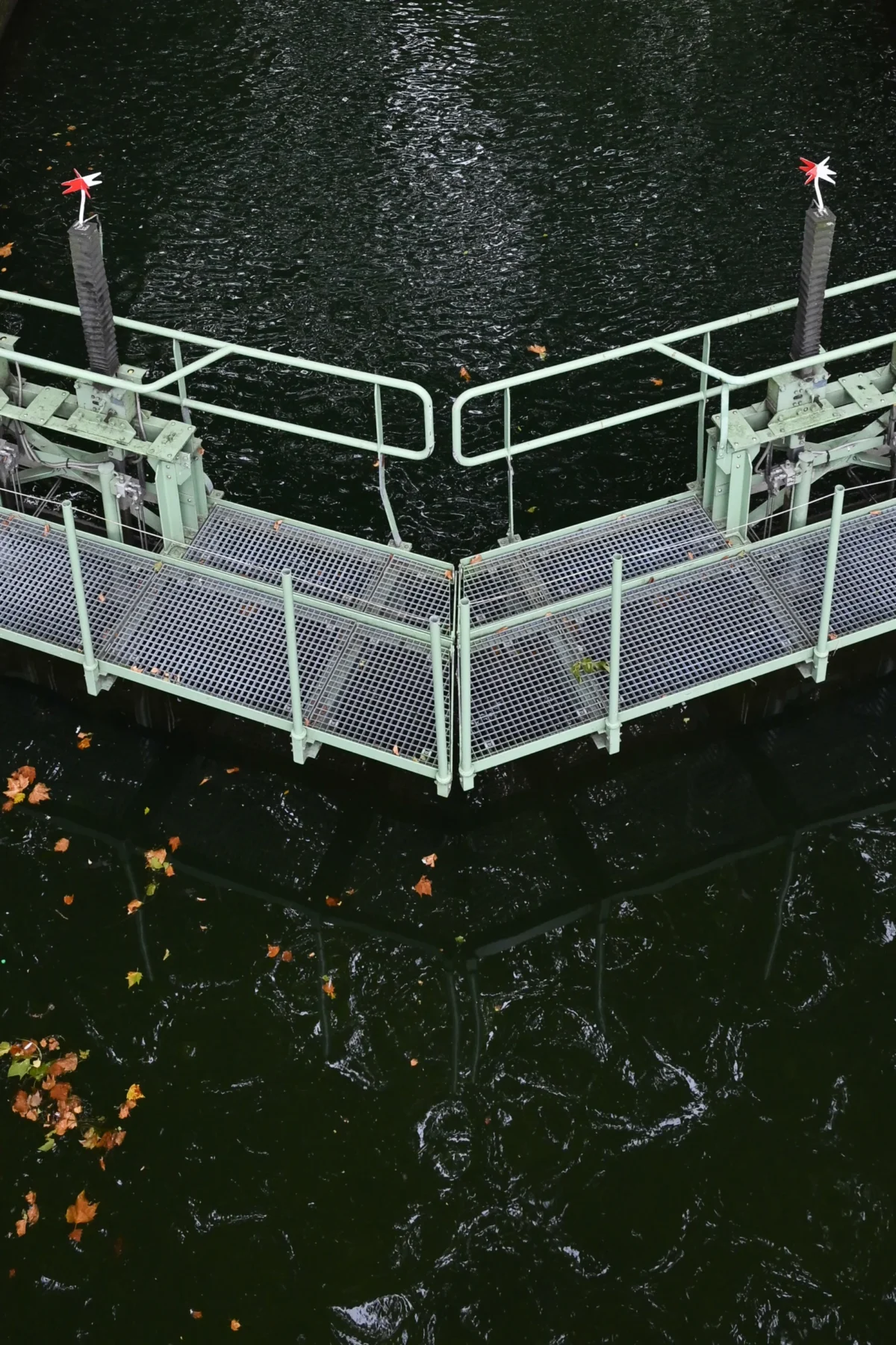 Jean-Marc · 13/09/2025 · 2095 x 3143 Cette photographie montre une structure métallique en forme de ponton ou de passerelle flottante, entourée d’un filet. Le sujet principal est cette installation, probablement utilisée pour la pêche ou la protection d’un espace aquatique.La composition est symétrique, avec un cadrage serré sur la structure. La lumière, tamisée, crée des contrastes doux, accentuant les détails métalliques. Les couleurs dominantes sont les tons gris et verts métalliques, avec des reflets sombres de l’eau et quelques feuilles mortes en bas.L’ambiance est industrielle et fonctionnelle, évoquant une activité utilitaire en milieu aquatique.