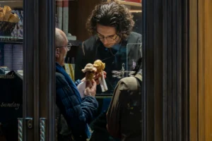 Jean-Marc · 20/12/2025 · 2860 x 1907 Cette photographie montre deux hommes dans un cadre intimiste, probablement un restaurant ou une cuisine. Le sujet principal semble être l’homme à droite, penché sur un plat qu’il examine attentivement, tandis que l’autre observe.La composition est serrée, avec un cadrage en plan rapproché. La lumière est douce et naturelle, éclairant les visages et les objets avec des ombres subtiles. Les couleurs dominantes sont les tons chauds (beige, brun) et les teintes froides (bleu du vêtement).Le style est réaliste et documentaire, créant une ambiance chaleureuse et immersive, presque théâtrale.
