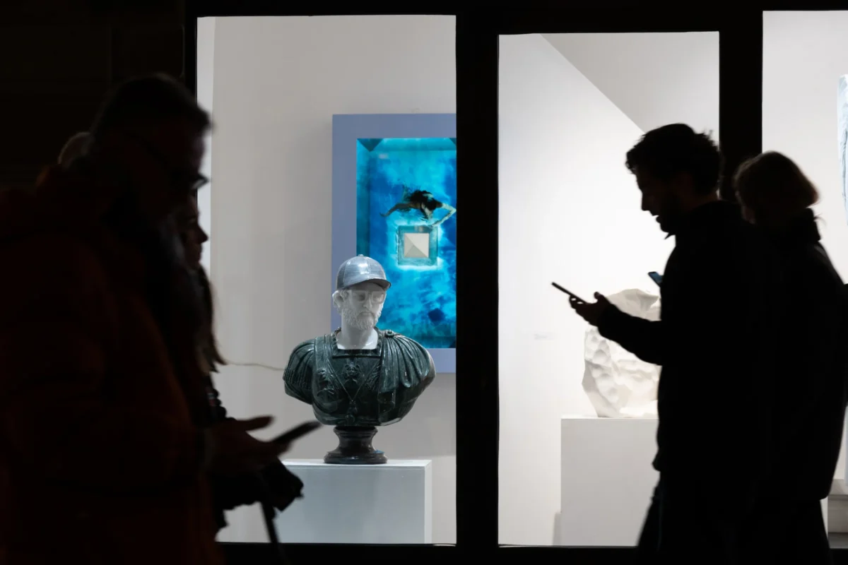 Jean-Marc · 20/12/2025 · 4042 x 2695 Cette photographie montre des visiteurs dans une galerie d'art moderne. Le sujet principal est une sculpture abstraite en forme de tête, posée sur un socle. La composition joue sur les contrastes entre les silhouettes des visiteurs et les éléments éclairés de l'exposition.Le cadrage est serré sur les œuvres et les personnes, créant une ambiance intimiste. La lumière est douce et dirigée, mettant en valeur les objets exposés. Les couleurs dominantes sont neutres (blanc, gris) avec des touches bleutées et des éclats lumineux.Le style est épuré et contemporain, évoquant une ambiance calme et réfléchie.