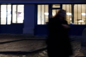 Thierry · 20/12/2025 · 3840 x 2560 Cette photographie présente un sujet flou en mouvement, probablement une personne vêtue de noir. La composition est simple, avec un cadrage serré sur le sujet devant un bâtiment aux fenêtres éclairées. La lumière est tamisée, créant une ambiance nocturne ou crépusculaire. Les couleurs dominantes sont les bleus froids du bâtiment et les teintes sombres du sujet, renforçant une atmosphère mystérieuse et légèrement mélancolique. Le style est minimaliste et réaliste, avec un flou de mouvement qui ajoute une touche dynamique. L’ambiance générale est intimiste et un peu énigmatique.