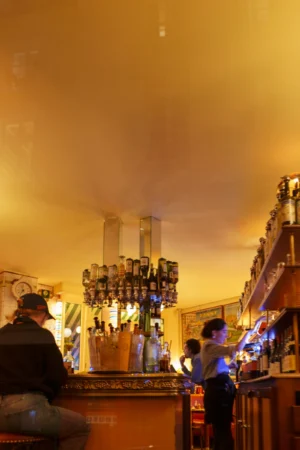 Thierry · 20/12/2025 · 2560 x 3840 Cette photographie capture une scène nocturne animée dans un bar ou un restaurant. Le sujet principal semble être un groupe de personnes autour d’un comptoir éclairé, probablement un bar à cocktails.La composition montre une ambiance conviviale et dynamique, avec des clients et des serveurs en activité. Le cadrage est serré, mettant en valeur les détails des lumières et des interactions. Les couleurs dominantes sont des tons chauds (oranges, jaunes) créant une ambiance chaleureuse et tamisée, renforcée par des éclairages artificiels bleutés.Le style est réaliste et spontané, évoquant une ambiance nocturne festive et intimiste.