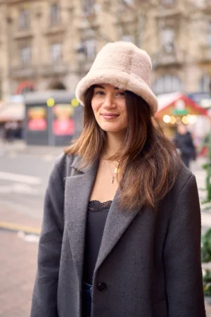 Gief · 1080 x 1620 Cette photographie met en scène une jeune femme comme sujet principal, souriante et élégante. Elle porte un manteau gris et un chapeau en laine beige, avec des cheveux longs et lisses.La composition est simple et centrée, avec un cadrage serré sur elle. L’arrière-plan flou montre une rue animée, avec des bâtiments et des couleurs vives.La lumière est naturelle et douce, probablement en journée. Les couleurs dominantes sont les tons neutres (gris, beige) contrastant avec les couleurs vives de l’arrière-plan.Le style est naturel et urbain, évoquant une ambiance chaleureuse et décontractée.