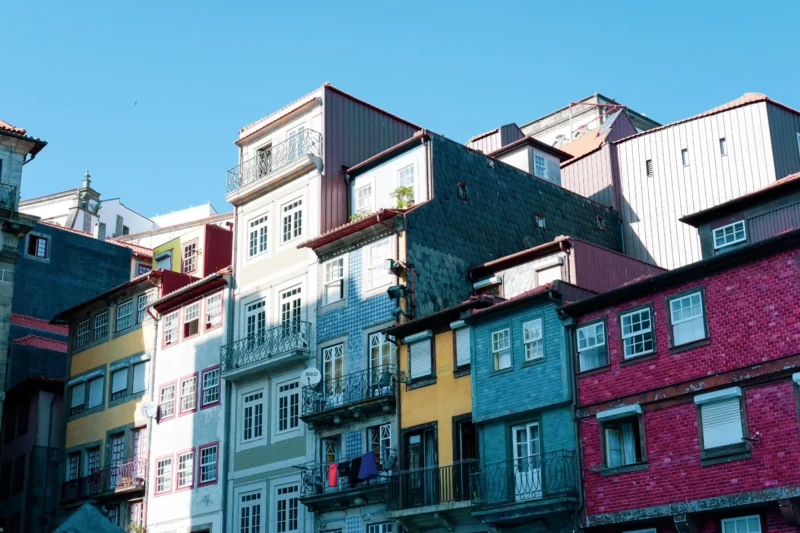 Romain · 09/08/2025 · 1776 x 1184 Cette photographie met en scène une rangée de bâtiments colorés et variés, typiques d’un quartier urbain vibrant. Le sujet principal est cette architecture éclectique, aux façades aux teintes vives et contrastées.La composition est serrée, avec un cadrage en contre-plongée qui accentue la hauteur des immeubles. La lumière, naturelle et douce, semble provenir d’un angle latéral, créant des ombres légères et mettant en valeur les couleurs.Les couleurs dominantes sont vives : bleu, rouge, jaune, vert et gris, offrant une ambiance joyeuse et dynamique. Le style rappelle l’art déco ou une esthétique postmoderne. L’ambiance est à la fois moderne et chaleureuse, évoquant un lieu de vie animé.