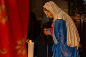 Marc · 20/12/2025 · 6045 x 4045 Cette photographie montre une scène religieuse ou théâtrale. Le sujet principal est une personne vêtue d’un habit bleu et blanc, probablement une représentation de la Vierge Marie, penchée vers une enfant en noir.La composition est serrée, centrée sur les deux figures. Le cadrage est rapproché, mettant en valeur les expressions et les détails des vêtements. La lumière est douce et naturelle, créant une ambiance chaleureuse et solennelle. Les couleurs dominantes sont les bleus, blancs et noirs, avec des touches de rouge en arrière-plan.Le style évoque une scène traditionnelle et émouvante, renforçant une ambiance de dévotion ou de représentation sacrée.