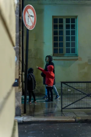 Marc · 20/12/2025 · 4672 x 7008 Cette photographie capture deux enfants comme sujets principaux, l’un en rouge vif et l’autre en noir, traversant une rue sous une pluie légère. La composition est dynamique, avec un cadrage serré qui isole les enfants du reste de l’environnement.Les couleurs dominantes sont les tons froids et gris de la pluie, contrastant avec le rouge éclatant du vêtement de l’enfant. La lumière est tamisée, créant une ambiance sombre et légèrement mélancolique. Le style est réaliste et documentaire, évoquant une scène de vie quotidienne. L’ambiance est intimiste et poétique, renforcée par les reflets sur le sol mouillé.