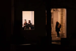 Deniz · 20/12/2025 · 2048 x 1365 Cette photographie met en scène une ambiance nocturne mystérieuse. Le sujet principal semble être les silhouettes reflétées dans une vitre, éclairées par une lumière douce en arrière-plan. La composition joue sur le contraste entre l’obscurité de l’avant-plan et la lumière tamisée de l’intérieur.Le cadrage est serré, centré sur la vitre et les reflets, créant une impression d’intimité et d’isolement. Les couleurs dominantes sont les tons sombres et les teintes chaudes de la lumière artificielle, renforçant une ambiance nocturne et contemplative. Le style est réaliste et sobre, évoquant une atmosphère poétique et mélancolique.