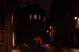 Deniz · 20/12/2025 · 2048 x 1365 Cette photographie capture une ruelle urbaine nocturne. Le sujet principal est une silhouette floue au centre, évoquant une personne en mouvement. La composition est symétrique avec des bâtiments sombres de chaque côté, créant un couloir étroit.Le cadrage est serré, mettant en valeur la profondeur et l'isolement. La lumière est faible, avec des teintes chaudes et froides contrastées : des ombres dominantes et des éclairages jaunâtres provenant des réverbères. Les couleurs sont principalement des noirs et gris, avec des touches de bleu et jaune.L'ambiance est mystérieuse et légèrement inquiétante, renforcée par le style sombre et le flou artistique.