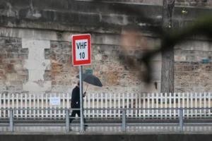 Pierre · 20/12/2025 · 2656 x 1767 Cette photographie met en scène un panneau routier "VHF 10" en premier plan, partiellement occulté par une ombre. Le sujet principal est une silhouette floue d’une personne tenant un parapluie noir, marchant sous une pluie fine. La composition joue sur les contrastes entre le premier plan net et l’arrière-plan flou.Le cadrage est serré, centré sur le panneau et la silhouette. La lumière est tamisée, créant une ambiance grise et humide. Les couleurs dominantes sont les tons froids (gris, noir, bleu pâle), renforçant une atmosphère mélancolique et urbaine. Le style est réaliste et documentaire.